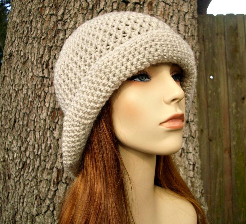 May include: A beige crocheted cloche hat with a wide brim. The hat is worn by a mannequin with long, red hair.