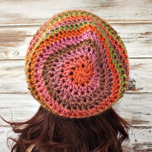 Puede incluir: Un gorro de punto de ganchillo en tonos marrones, rosas, naranjas y verdes. El gorro tiene un dise&ntilde;o circular con un patr&oacute;n de punto texturizado.