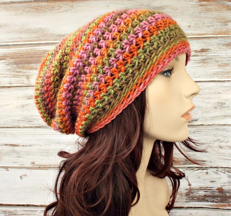 Puede incluir: Un gorro de punto de lana en crochet de estilo slouchy con un patr&oacute;n de rayas multicolor de verde, naranja, rosa y marr&oacute;n.