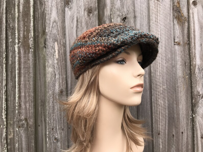 Op de afbeelding: Een gebreide newsboy-pet in bruin, teal en oranje. De pet heeft een platte bovenkant en een gebogen rand.
