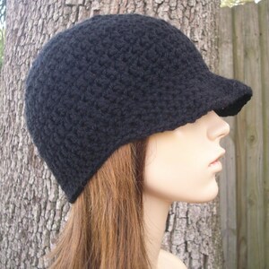 May include: A black crocheted beanie with a brim. The beanie is worn on a mannequin with long brown hair.