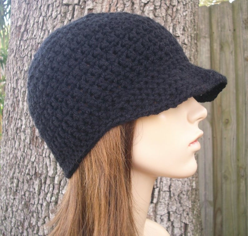 May include: A black crocheted beanie with a brim. The beanie is worn on a mannequin with long brown hair.