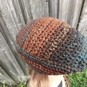 Op de afbeelding: Een gebreide beanie met een bruine, oranje en blauwe kleurverloop. De beanie is gemaakt met een textuur steek.