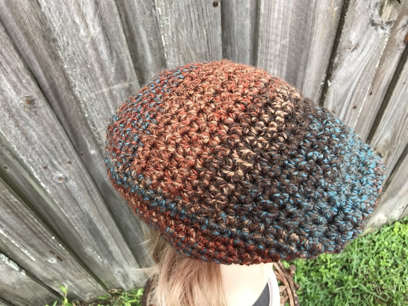 Op de afbeelding: Een gebreide beanie met een bruine, oranje en blauwe kleurverloop. De beanie is gemaakt met een textuur steek.