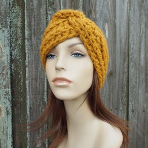 K&ouml;nnte beinhalten: Ein geh&auml;keltes Stirnband in Senfgelb mit einem geknoteten Design. Das Stirnband wird von einer Mannequin mit langen braunen Haaren getragen.