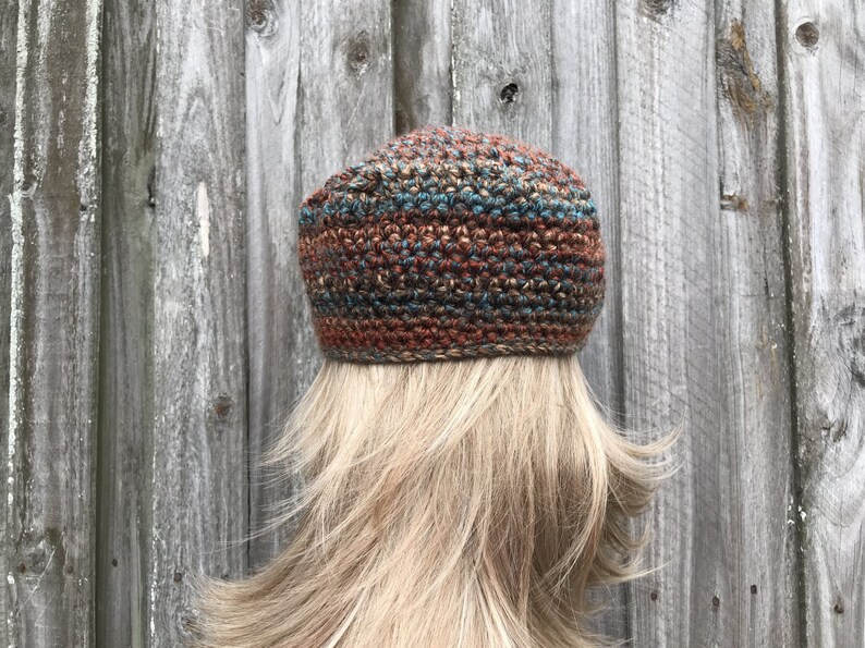 Op de afbeelding: Een gebreide beanie met een bruin, blauw en beige gestreept patroon. De beanie is gemaakt van een getextureerd garen en heeft een slouchy pasvorm.