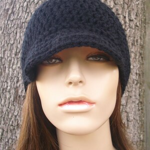 May include: A black crocheted beanie with a brim. The beanie is worn on a mannequin with long brown hair.