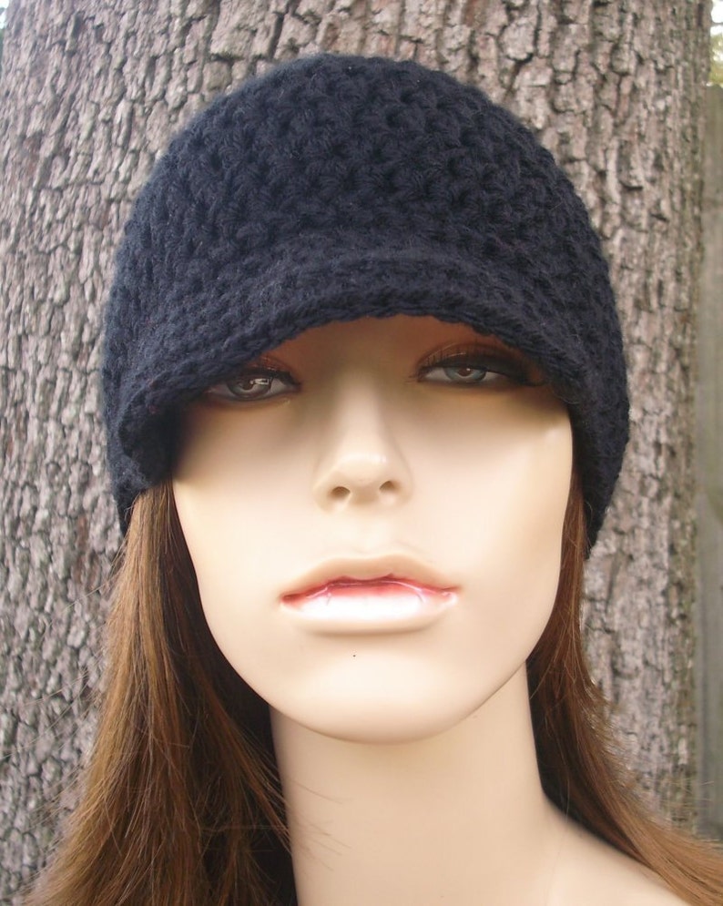 May include: A black crocheted beanie with a brim. The beanie is worn on a mannequin with long brown hair.