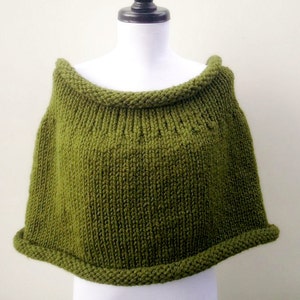 May include: A green knitted poncho with a wide, folded collar. The poncho is made of a soft, textured yarn and has a simple, classic design.