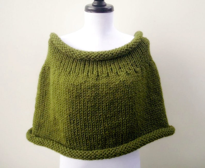 May include: A green knitted poncho with a wide, folded collar. The poncho is made of a soft, textured yarn and has a simple, classic design.