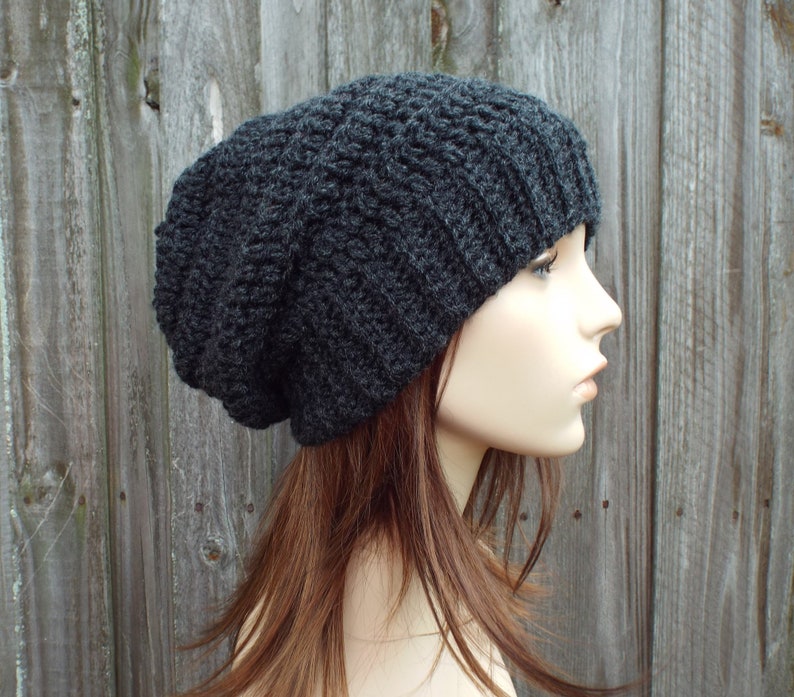 May include: A dark gray, slouchy beanie hat. The hat is made of a thick, textured yarn with a ribbed brim. The hat is shown on a mannequin head, with the side profile visible.