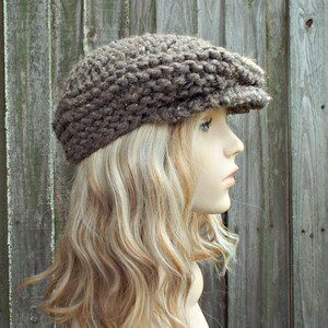 May include: A brown, chunky knit newsboy cap featuring a textured, thick yarn construction with a short, stiff brim. The hat has a rounded, voluminous crown and a fitted band, showcasing a rustic, multi-tonal brown color palette throughout.