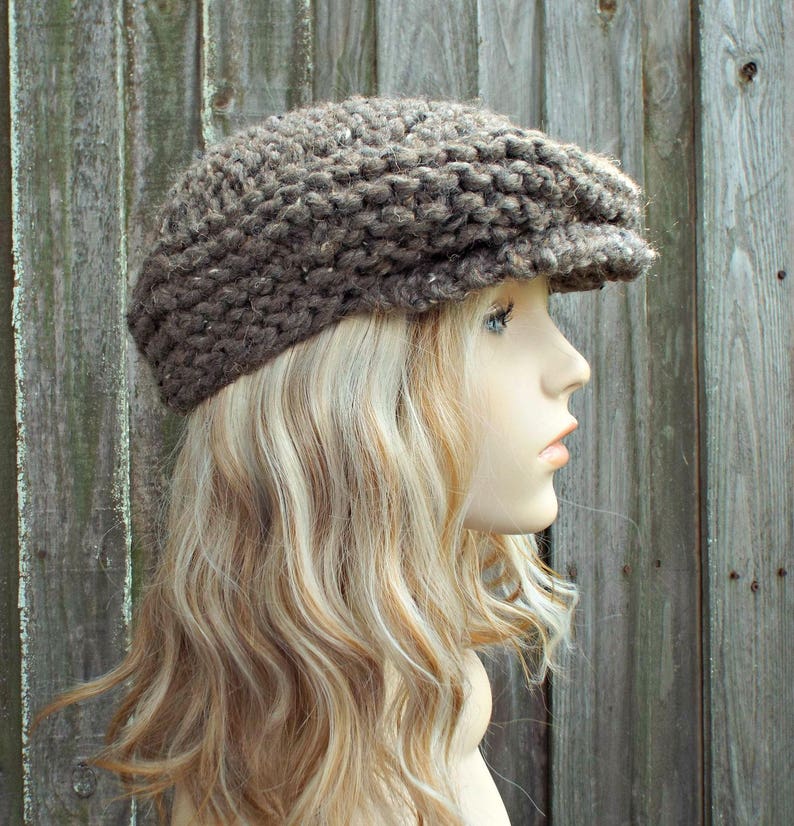 May include: A brown, chunky knit newsboy cap featuring a textured, thick yarn construction with a short, stiff brim. The hat has a rounded, voluminous crown and a fitted band, showcasing a rustic, multi-tonal brown color palette throughout.