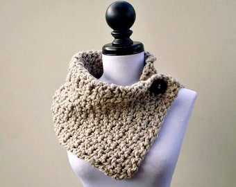May include: A beige crocheted cowl with a single button closure. The cowl is displayed on a white mannequin.