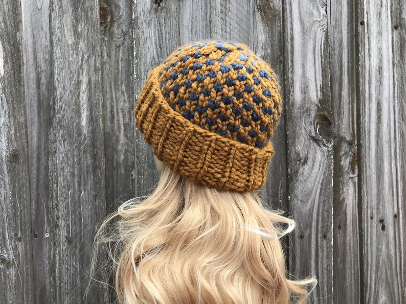 May include: A knitted beanie hat with a mustard yellow and dark blue geometric pattern. The hat is made with a chunky yarn and has a fold-over brim.