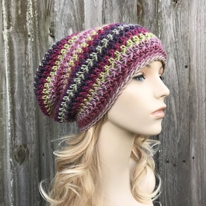 Puede incluir: Un gorro de punto de ganchillo holgado en un patr&oacute;n de rayas multicolores de rosa, morado, verde y marr&oacute;n.