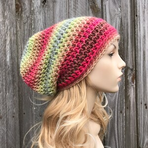 Puede incluir: Un gorro de punto de ganchillo holgado con un patr&oacute;n de degradado multicolor de rosa, rojo, marr&oacute;n, verde y gris.