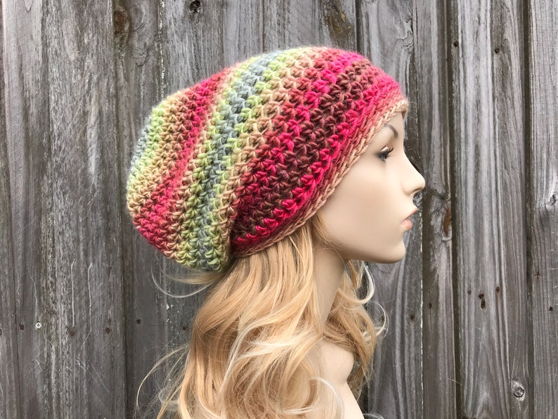 Puede incluir: Un gorro de punto de ganchillo holgado con un patr&oacute;n de degradado multicolor de rosa, rojo, marr&oacute;n, verde y gris.