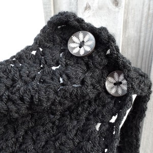 May include: Black crocheted cowl with two decorative buttons featuring a white floral design.