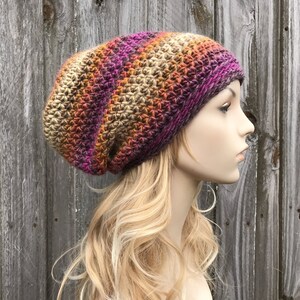 Puede incluir: Un gorro de punto de ganchillo holgado con un patr&oacute;n de degradado multicolor de marr&oacute;n, naranja, rosa y morado.