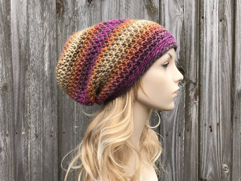 Puede incluir: Un gorro de punto de ganchillo holgado con un patr&oacute;n de degradado multicolor de marr&oacute;n, naranja, rosa y morado.