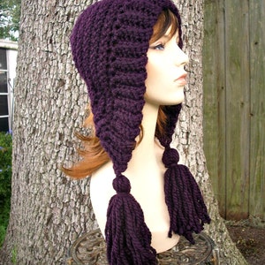 Puede incluir: Sombrero de punto de color morado con una corona larga y puntiaguda y dos borlas largas. El sombrero est&aacute; hecho con un punto texturizado y se lleva en un maniqu&iacute;.