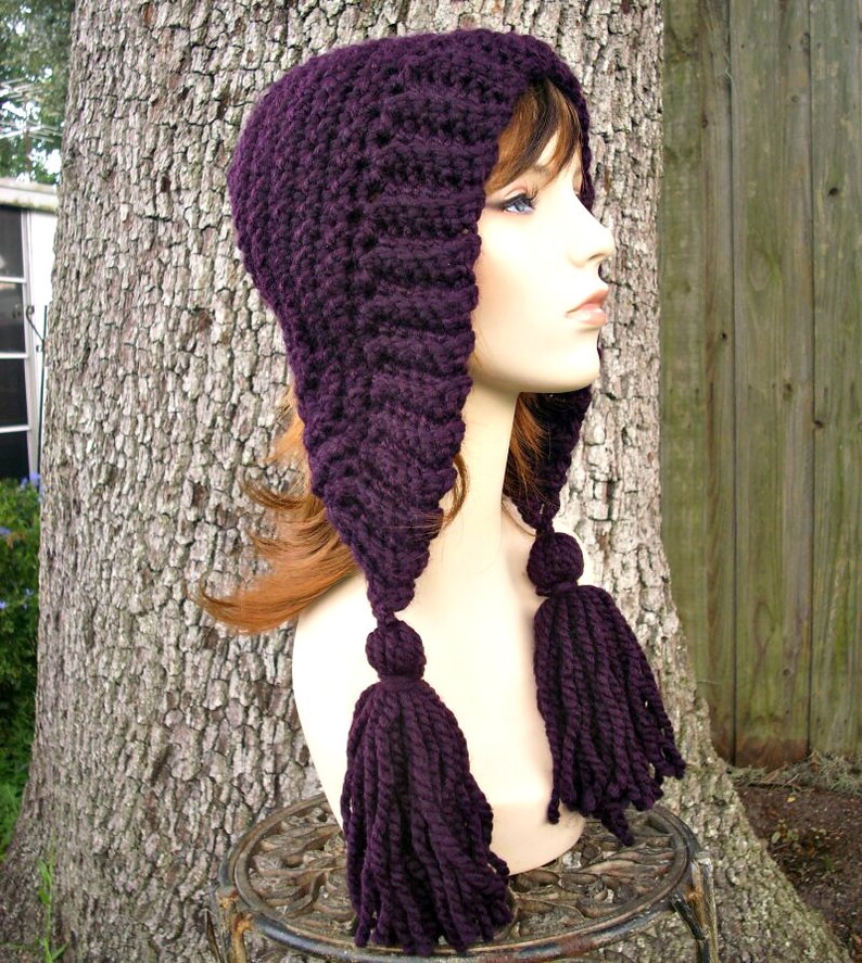 Puede incluir: Sombrero de punto de color morado con una corona larga y puntiaguda y dos borlas largas. El sombrero est&aacute; hecho con un punto texturizado y se lleva en un maniqu&iacute;.