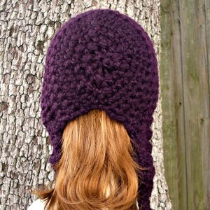 Puede incluir: Un gorro de punto de color morado con largas orejeras. El gorro est&aacute; hecho con un hilo grueso y tiene un patr&oacute;n de punto texturizado.