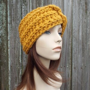 K&ouml;nnte beinhalten: Ein geh&auml;keltes Stirnband in Senfgelb mit einem gefalteten Design. Das Stirnband wird von einer Mannequin mit braunen Haaren getragen.