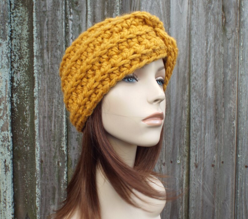 K&ouml;nnte beinhalten: Ein geh&auml;keltes Stirnband in Senfgelb mit einem gefalteten Design. Das Stirnband wird von einer Mannequin mit braunen Haaren getragen.