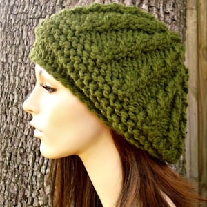 Könnte beinhalten: Eine grüne Strickmütze mit Zopfmuster. Die Mütze ist aus weichem Garn gefertigt und hat eine lockere Passform.