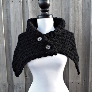 May include: Black crocheted cowl with a button closure. The cowl is made of a soft, textured yarn and has a wide, flowing shape.