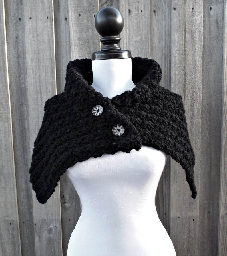 May include: Black crocheted cowl with a button closure. The cowl is made of a soft, textured yarn and has a wide, flowing shape.