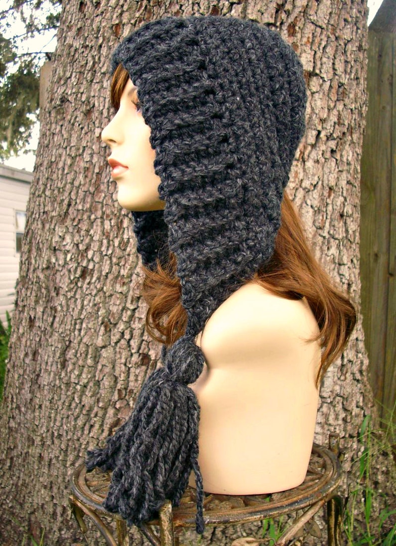 May include: A gray crocheted hooded hat with a long tassel. The hat is made of a soft, chunky yarn and has a simple, classic design.