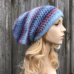 Puede incluir: Un gorro beanie holgado con un patr&oacute;n de rayas azules, moradas y rosas. El gorro est&aacute; tejido a crochet y tiene un ajuste holgado y relajado.