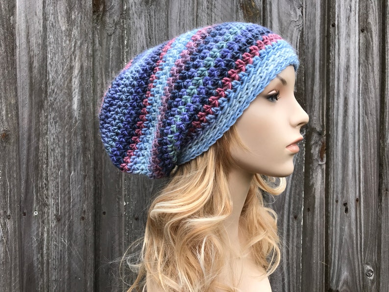 Puede incluir: Un gorro beanie holgado con un patr&oacute;n de rayas azules, moradas y rosas. El gorro est&aacute; tejido a crochet y tiene un ajuste holgado y relajado.