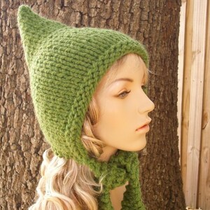 May include: A green knitted hat with a pointed top and a matching scarf. The hat has a long, pointed ear flap on each side.