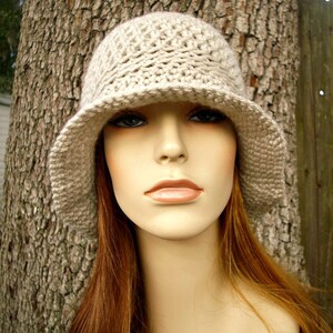 May include: A beige crocheted hat with a wide brim. The hat is worn by a mannequin with long, straight, reddish-brown hair.