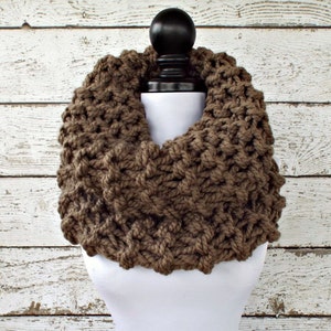May include: A brown knitted infinity scarf with a chunky knit texture. The scarf is displayed on a white mannequin.