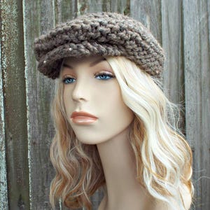 May include: A brown chunky knit newsboy cap featuring a thick, textured yarn construction with a prominent brim. The hat is crafted with a visible, repeating stitch pattern that creates a dense, warm appearance, covering the top of the head.
