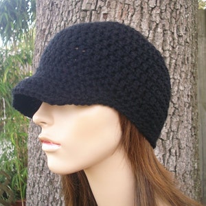 May include: A black crocheted beanie with a brim. The beanie is worn on a mannequin with long brown hair.