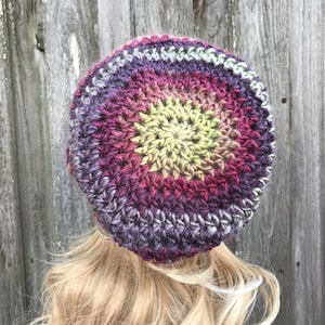 Puede incluir: Un gorro de punto de ganchillo con un dise&ntilde;o degradado de colores en tonos de morado, rosa, amarillo y verde. El gorro est&aacute; hecho con un hilo grueso y tiene un ajuste holgado.
