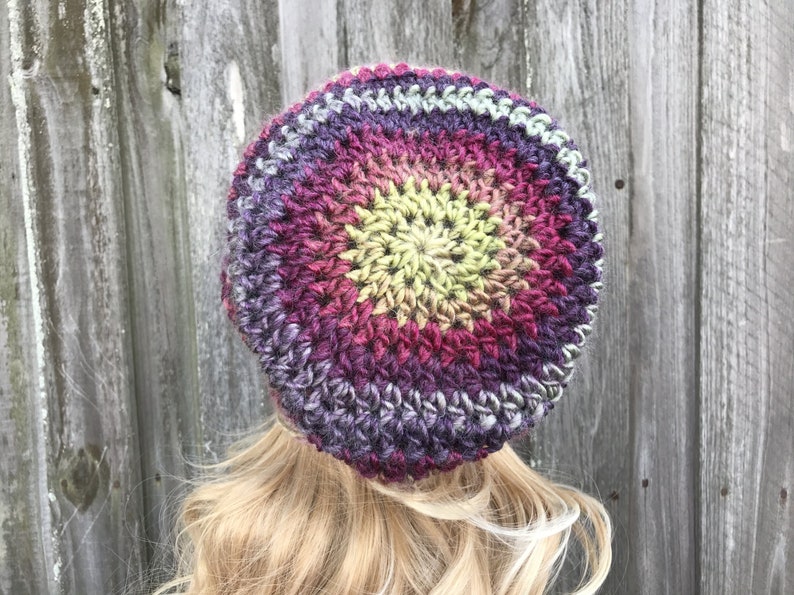 Puede incluir: Un gorro de punto de ganchillo con un dise&ntilde;o degradado de colores en tonos de morado, rosa, amarillo y verde. El gorro est&aacute; hecho con un hilo grueso y tiene un ajuste holgado.