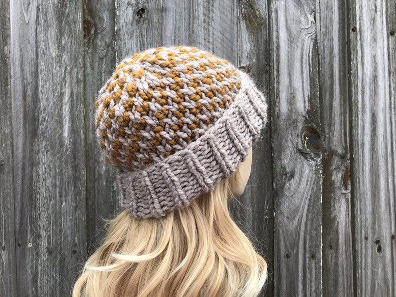 May include: A knitted beanie hat in a light grey and mustard yellow color combination. The hat has a ribbed brim and a textured pattern.