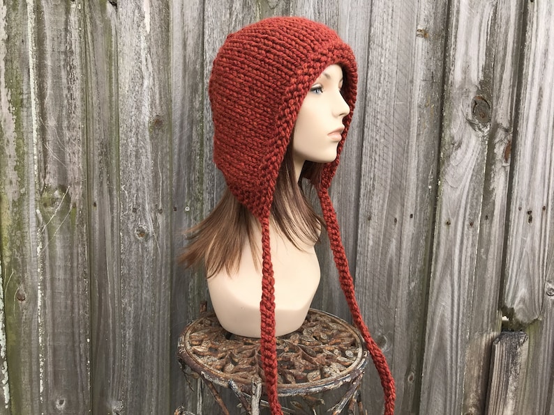 A chunky knit bonnet with i-cord ties. This hat comes in 33 colors, shown here in spice, a burnt orange. This hat fits an average adult and teen head size of 20 to 23 inches.