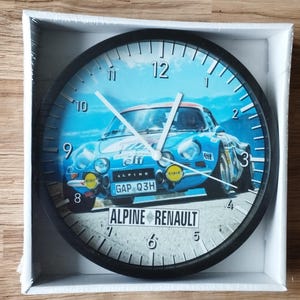 Può includere: Un orologio da parete nero con un'immagine blu e bianca di un'auto da corsa d'epoca. Il quadrante dell'orologio ha numeri e lancette neri. L'auto è etichettata "Alpine Renault" e "Elf".