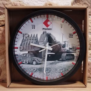 Puede incluir: Reloj en blanco y negro con un logotipo de Poclain rojo y blanco. La esfera del reloj presenta una imagen en blanco y negro de una excavadora Poclain y un coche antiguo.