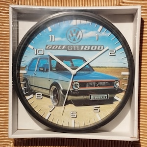 Puede incluir: Reloj de pared negro con una esfera blanca y agujas negras. La esfera del reloj presenta una imagen de un Volkswagen Golf GTI 1800 plateado con un cielo azul y nubes blancas en el fondo. La esfera del reloj también tiene números negros y el texto "GOLF GTI 1800".