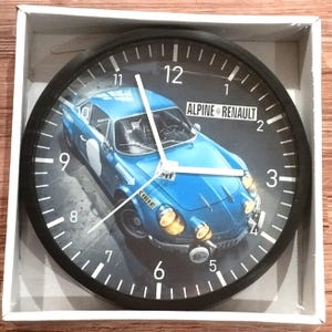 Könnte beinhalten: Eine Wanduhr mit schwarzem Rahmen und einem Bild eines blauen und weißen Alpine Renault Autos. Das Zifferblatt der Uhr hat schwarze Zahlen und weiße Markierungen.