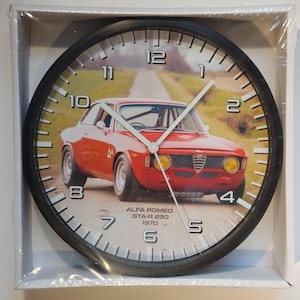 Peut inclure: Horloge murale ronde avec un cadre noir. Le cadran présente une voiture rouge Alfa Romeo GTA-R 290 de 1970 sur une route. Aiguilles blanches et chiffres noirs. L'horloge est dans une boîte blanche. Diamètre d'environ 25 cm.